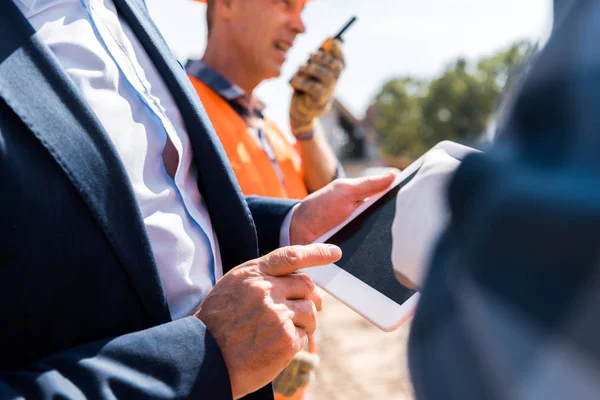 Обрезанный вид бизнесмена, указывающего пальцем на цифровой планшет рядом с архитекторами — стоковое фото