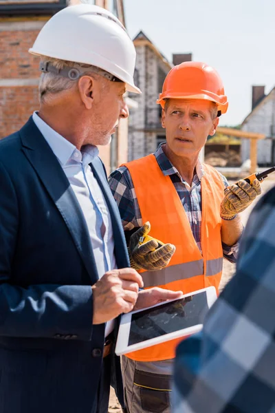 Enfoque selectivo del constructor mirando al hombre de negocios barbudo mientras sostiene walkie talkie - foto de stock