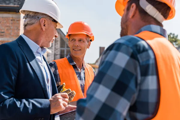 Foyer sélectif du constructeur regardant barbu homme d'affaires près de son collègue — Photo de stock