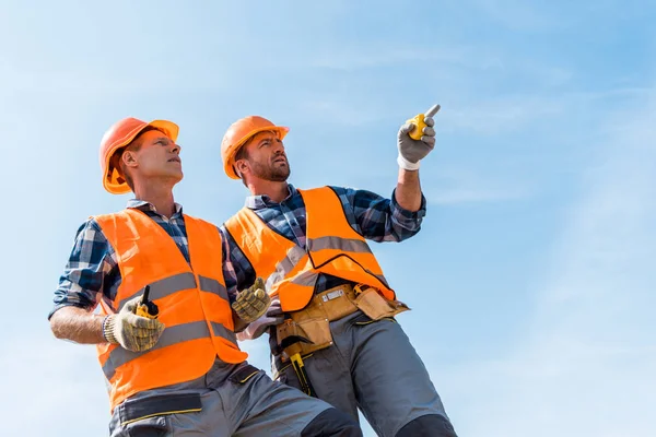 Tiefansicht des gutaussehenden Bauunternehmers, der mit dem Finger zeigt, während er vor blauem Himmel steht — Stockfoto