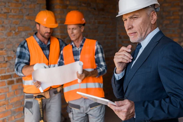 Selective focus of mature businessman holding digital tablet near architects — Stock Photo