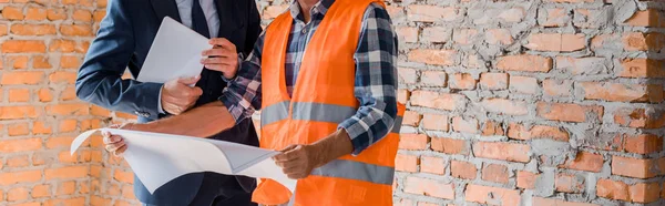 Panoramic shot of architect holding blueprint near businessman with digital tablet — Stock Photo
