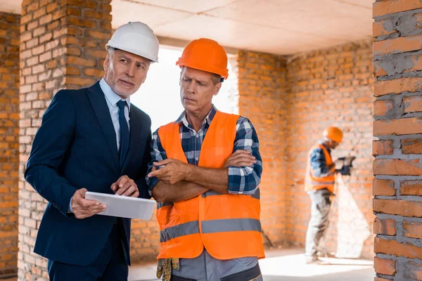 Selective focus of businessman standing near builder pointing with finger at digital tablet — Stock Photo