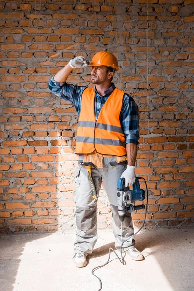 Handsome bearded man holding hammer drill while touching helmet — Stock Photo