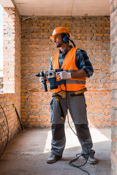 Handsome bearded man holding hammer drill near brick walls — Stock Photo
