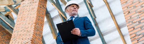 Panoramic shot of businessman in helmet holding clipboard — Stock Photo