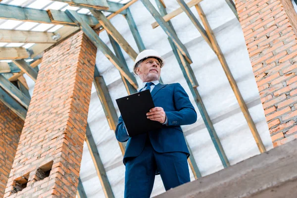Vista de ángulo bajo del hombre de negocios en el casco portapapeles — Stock Photo