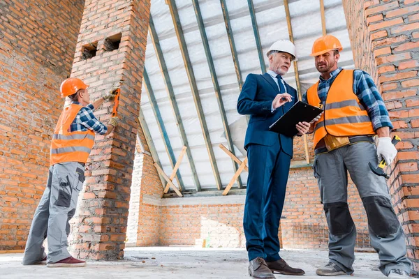 Зрілий бородатий бізнесмен тримає кишеню біля будівельників — стокове фото