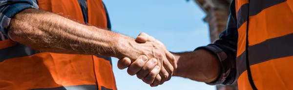 Colpo panoramico di uomini che stringono la mano contro il cielo blu — Foto stock