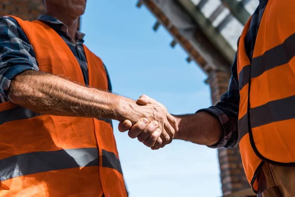 Vista ritagliata di uomini che stringono la mano contro il cielo blu — Stock Photo