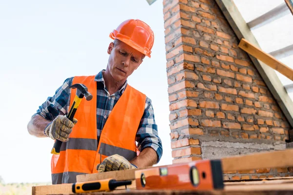 Enfoque selectivo del apuesto constructor de mediana edad sosteniendo el martillo - foto de stock