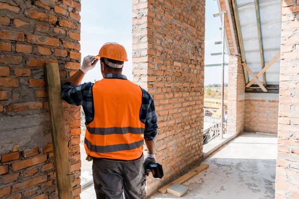 Back view of mature man holding hammer drill while standing near brick wall — Stock Photo