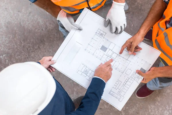 Top view of three men standing and pointing with fingers at blueprint — Stock Photo