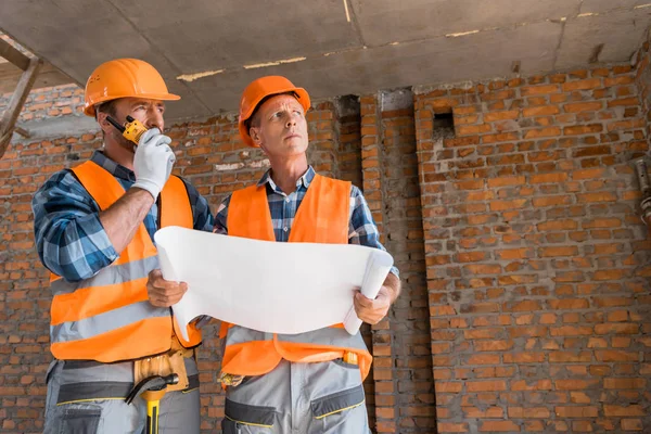 Costruttore in possesso di cianografia vicino bello collaboratore con walkie talkie — Foto stock