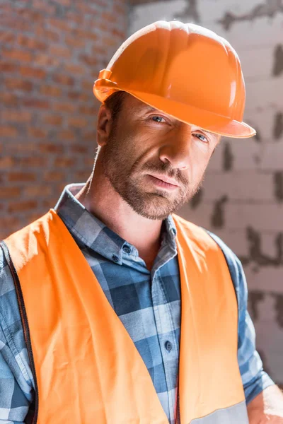 Hombre barbudo y guapo en casco naranja mirando a la cámara - foto de stock