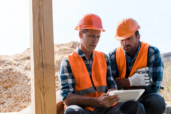 Guapo hombre de mediana edad sosteniendo tableta digital cerca de compañero de trabajo barbudo - foto de stock