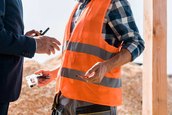 Visão cortada de empresário segurando walkie talkie perto construtor — Fotografia de Stock
