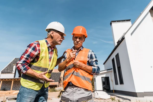 Middle aged constructors in helmets standing near houses — Stock Photo