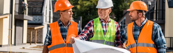 Panoramic shot of mature builder holding blueprint near coworkers — Stock Photo