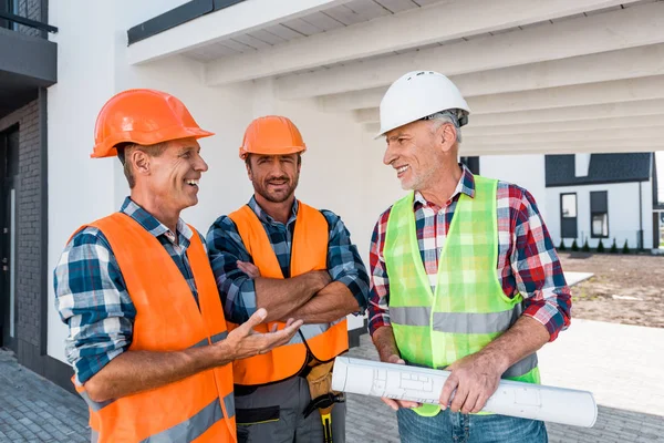 Constructeurs heureux dans les casques debout près de collègue avec le plan directeur — Photo de stock