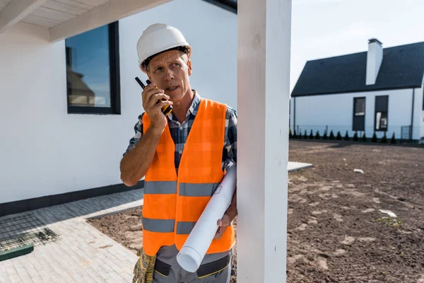 Mature man holding walkie talkie and blueprint near houses — Stock Photo