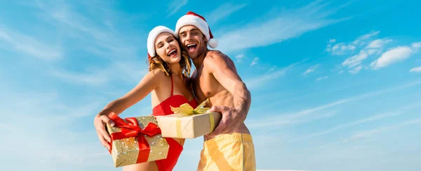 Plano panorámico de sexy y sonriente novia y novio sosteniendo regalos en la playa en Maldivas - foto de stock