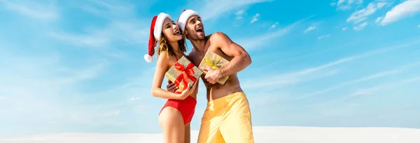 Tiro panorâmico de sexy e sorridente namorada e namorado segurando presentes na praia em Maldivas — Fotografia de Stock