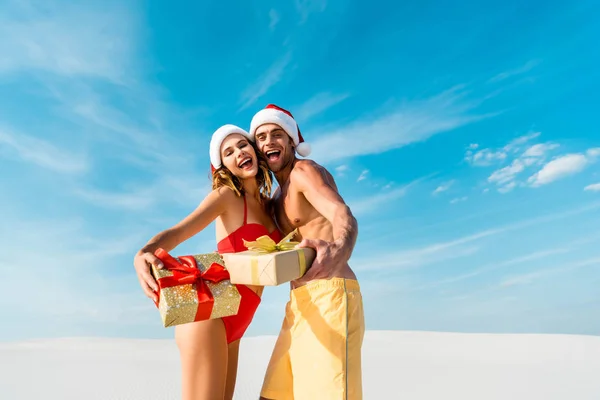 Sexy y sonriente novia y novio sosteniendo regalos en la playa en Maldivas - foto de stock