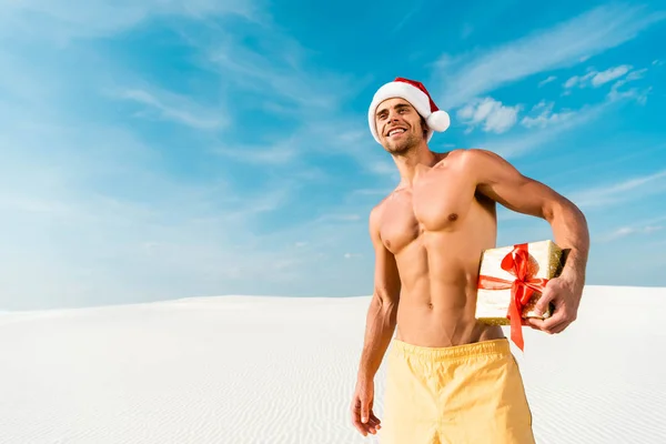 Uomo bello e sexy in cappello di Babbo Natale in possesso di regalo sulla spiaggia in Maldive — Foto stock