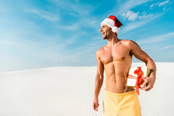 Homme beau et sexy chapeau santa tenant cadeau sur la plage aux Maldives — Photo de stock