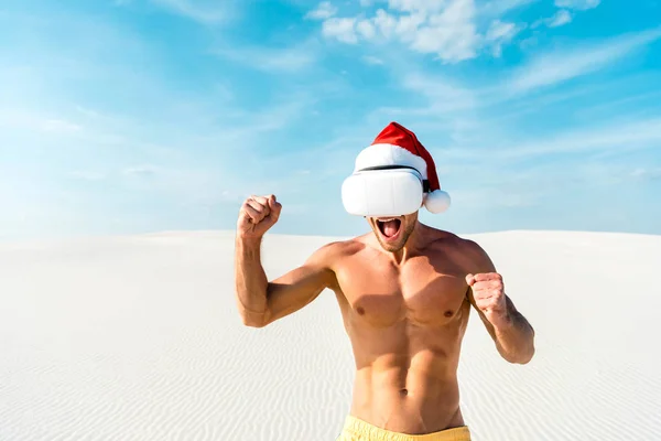 Homme sexy en santa chapeau avec casque de réalité virtuelle montrant oui geste sur la plage aux Maldives — Photo de stock