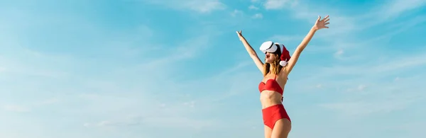 Colpo panoramico di donna sexy in cappello da Babbo Natale e costume da bagno con cuffia di realtà virtuale sulla spiaggia delle Maldive — Foto stock