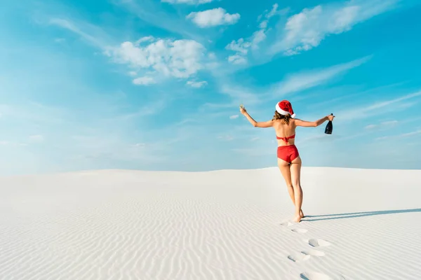 Vista trasera de la mujer sexy en sombrero de santa y traje de baño celebración de copa de champán y botella en la playa en Maldivas - foto de stock