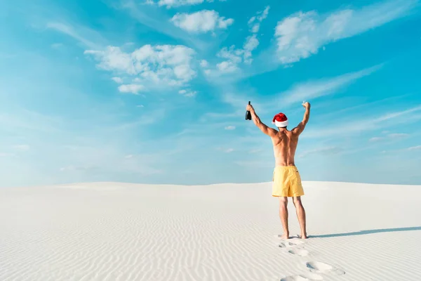 Vue arrière de l'homme sexy en santa chapeau tenant verre et bouteille sur la plage aux Maldives — Photo de stock