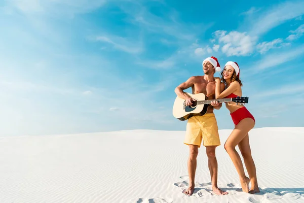 Panoramic shot of sexy girlfriend and boyfriend playing acoustic guitar on beach in Maldives — Stock Photo