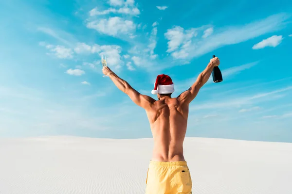 Vista trasera de hombre sexy en sombrero de santa celebración de vidrio y botella en la playa en Maldivas - foto de stock