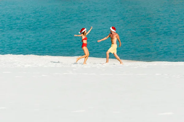 Сексуальная девушка и парень в шляпах Санты с протянутыми руками на пляже на Мальдивах — стоковое фото