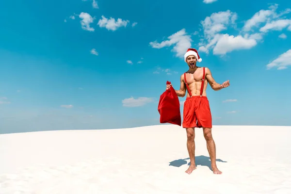 Shocked and sexy man in santa hat holding santa sack on beach in Maldives — Stock Photo