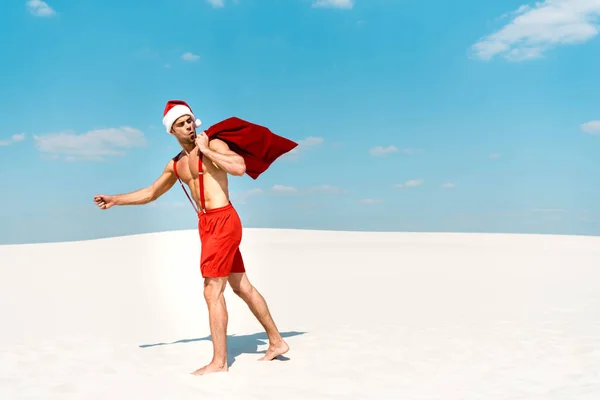 Handsome and sexy man in santa hat holding santa sack and walking on beach in Maldives — Stock Photo