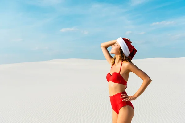 Mujer sexy y sonriente en sombrero de santa y traje de baño con los ojos cerrados en la playa en Maldivas - foto de stock