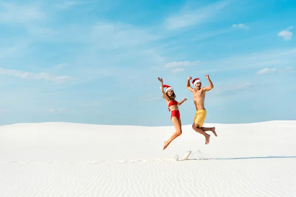 Namorada sexy e namorado em chapéus santa pulando na praia em Maldivas — Fotografia de Stock