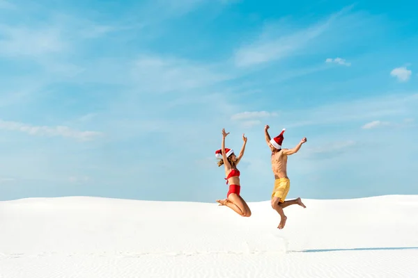 Namorada sexy e namorado em chapéus santa pulando na praia em Maldivas — Fotografia de Stock