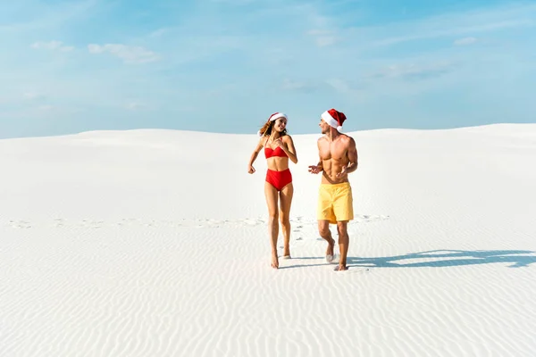 Sexy girlfriend and boyfriend in santa hats running on beach in Maldives — Stock Photo