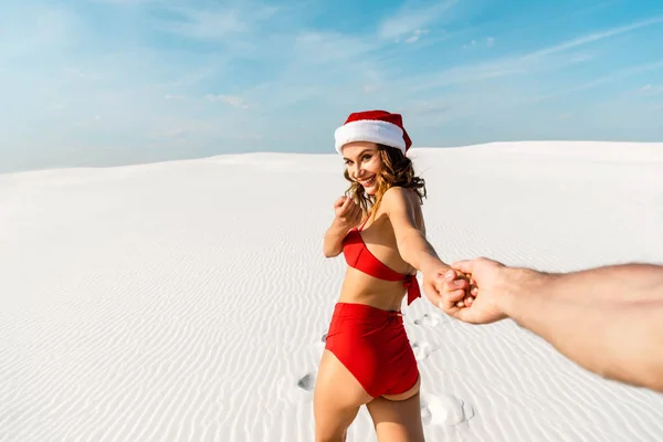 Vista ritagliata del fidanzato che tiene per mano la ragazza sexy in cappello di Babbo Natale sulla spiaggia in Maldive — Foto stock