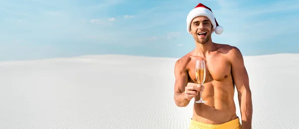 Tiro panorâmico de homem sexy em santa chapéu segurando taça de champanhe na praia em Maldivas — Fotografia de Stock