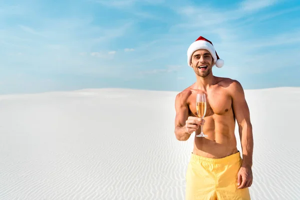 Sexy uomo in cappello di Babbo Natale in possesso di bicchiere di champagne sulla spiaggia in Maldive — Foto stock