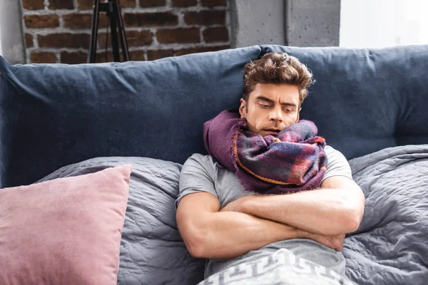 Sick and handsome man in scarf lying in bed — Stock Photo