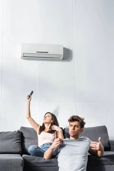 Attractive girlfriend switching on air conditioner and handsome boyfriend looking away — Stock Photo