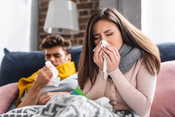 Selective focus of sick girlfriend sneezing and holding napkin — Stock Photo