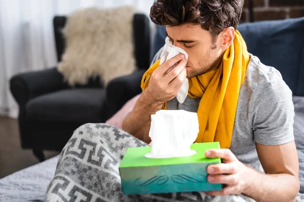 Enfermo en bufanda estornudando y sosteniendo la servilleta en el apartamento - foto de stock
